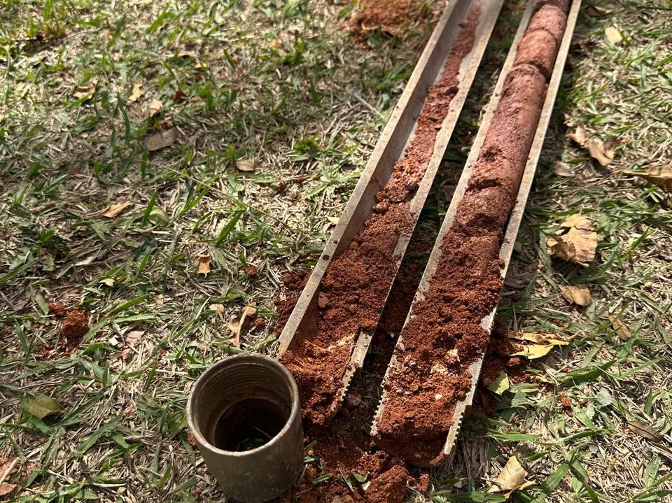Amostras de solo retiradas do furo, dispostas em meia-cana ao lado do amostrador padrão